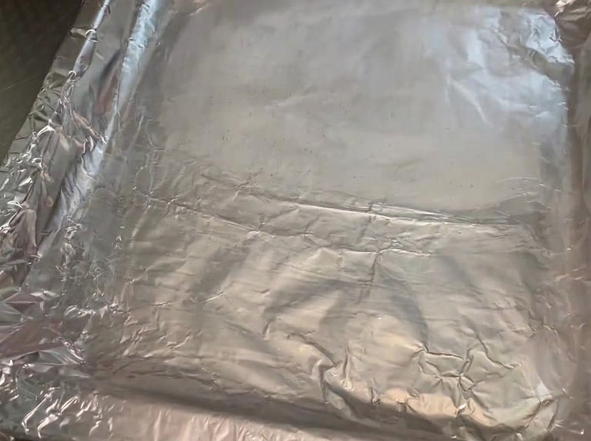 Una teglia di metallo rivestita di foglio di alluminio spiegazzato e spennellata con un denso strato di olio da cucina.