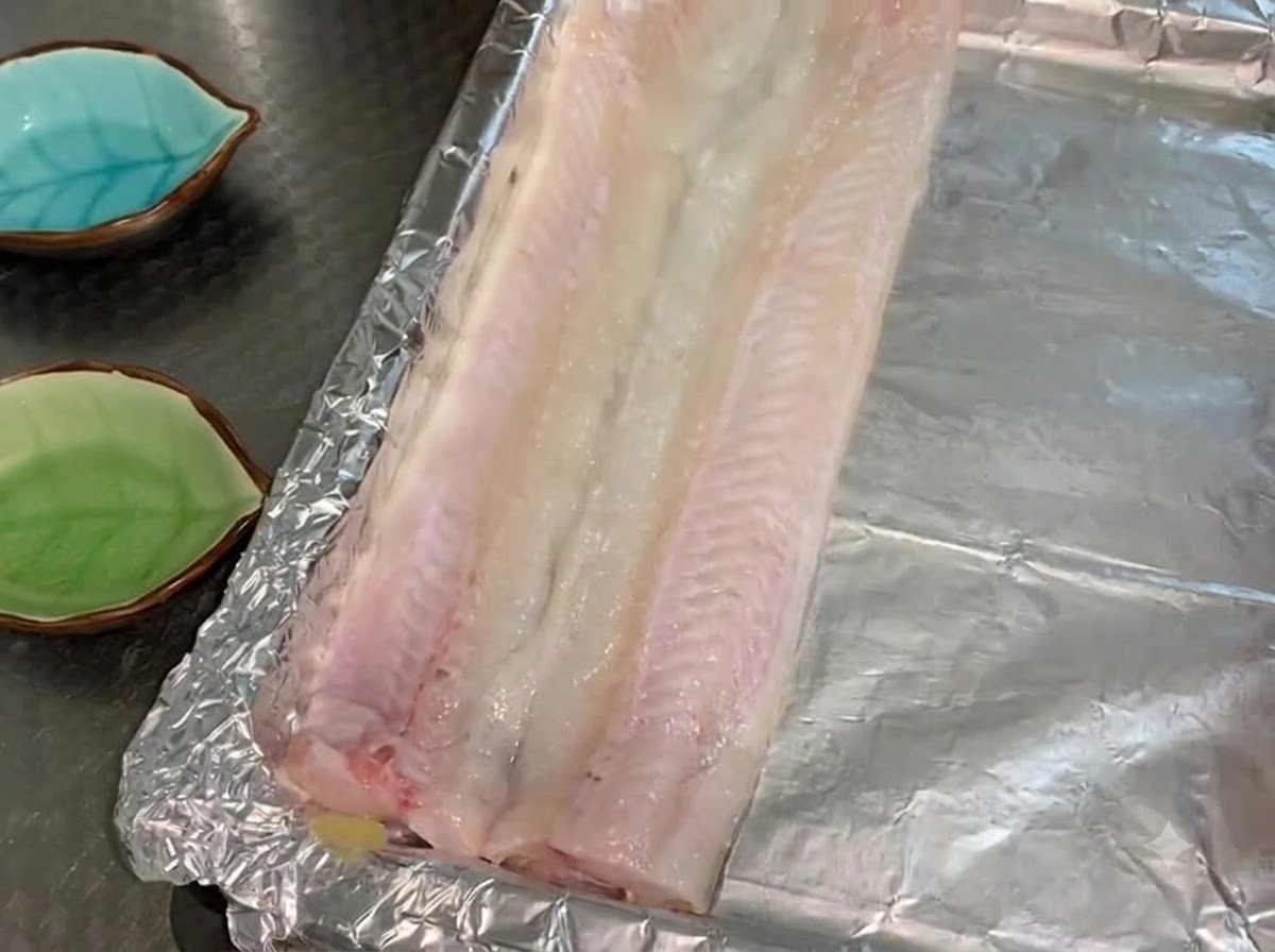 Filetti di anguilla cruda disposti in un unico strato su una teglia rivestita di alluminio e oliata.