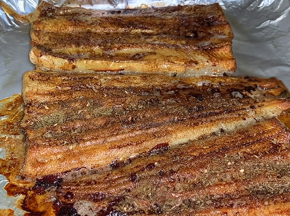 Filetti di anguilla cotta cosparsi uniformemente con uno strato di polvere di condimento BBQ marrone allinterno di una teglia.
