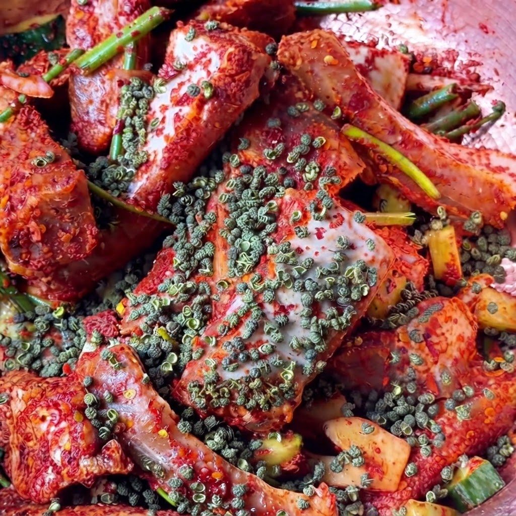 Una vista ravvicinata di grani di pepe rosso del Sichuan interi sparsi sui pezzi di carne rossa conditi.