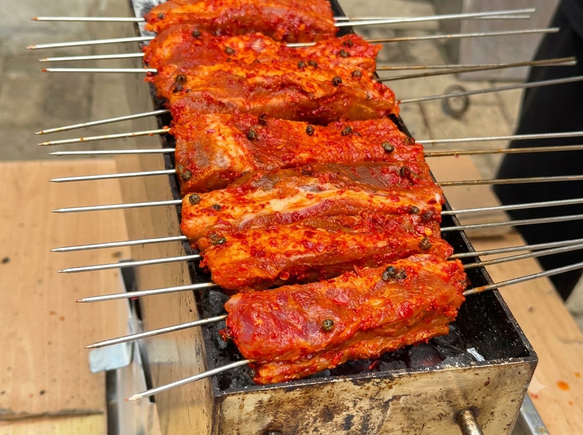 Molti spiedini di costine ricoperte di rosso allineati e in cottura su un braciere a carbone.