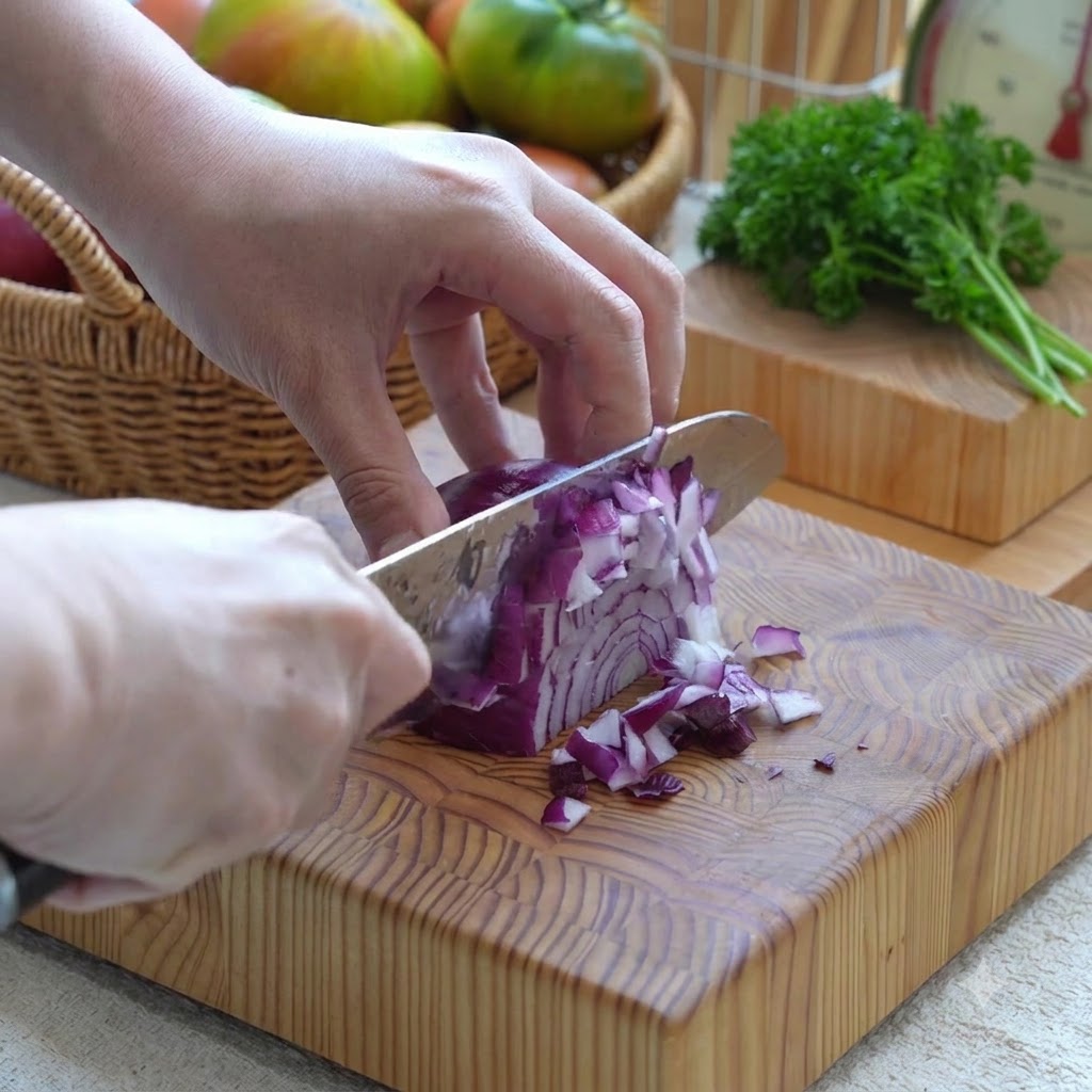 Cipolla rossa tagliata a cubetti piccoli con un coltello su un tagliere di legno.