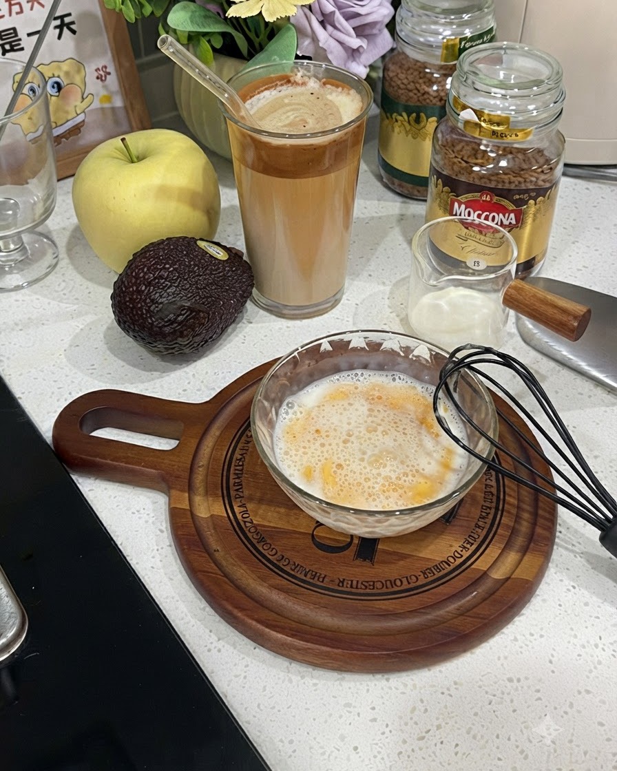 Una ciotola di vetro riempita con una miscela spumosa e sbattuta di uovo e latte accanto a una frusta nera.