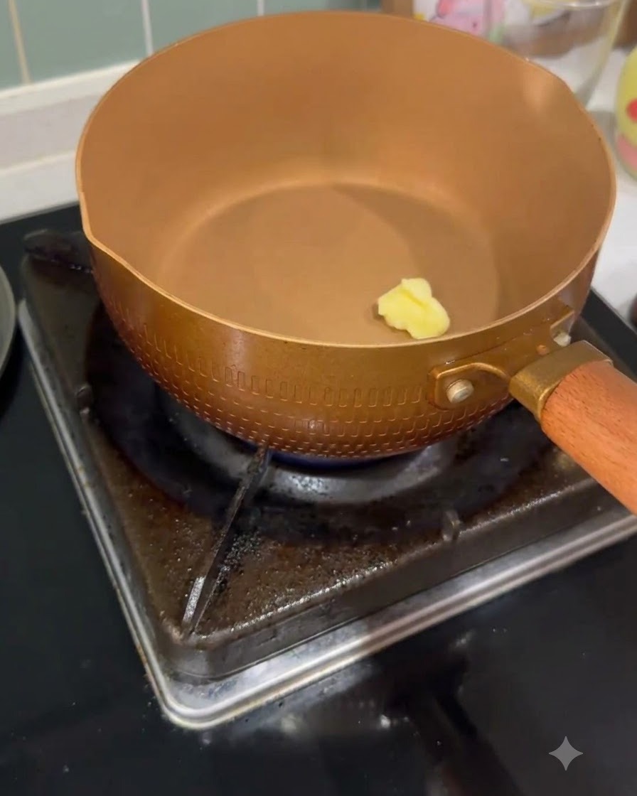 Una piccola noce di burro che si scioglie allinterno di una padella color rame riscaldata su un fornello a gas.