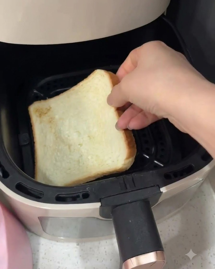 Una mano che posiziona una fetta di pane in cassetta bianco allinterno del cestello di una friggitrice ad aria.