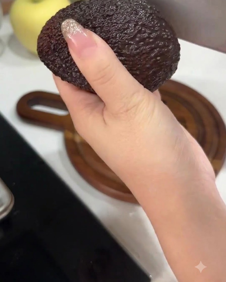 Una mano che tiene un avocado mentre lo taglia a metà con un grosso coltello da cucina.
