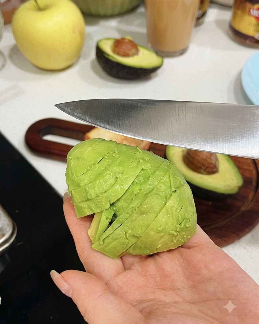 Una mano che tiene un avocado sbucciato a metà mentre un coltello da cucina lo taglia a pezzi uniformi.