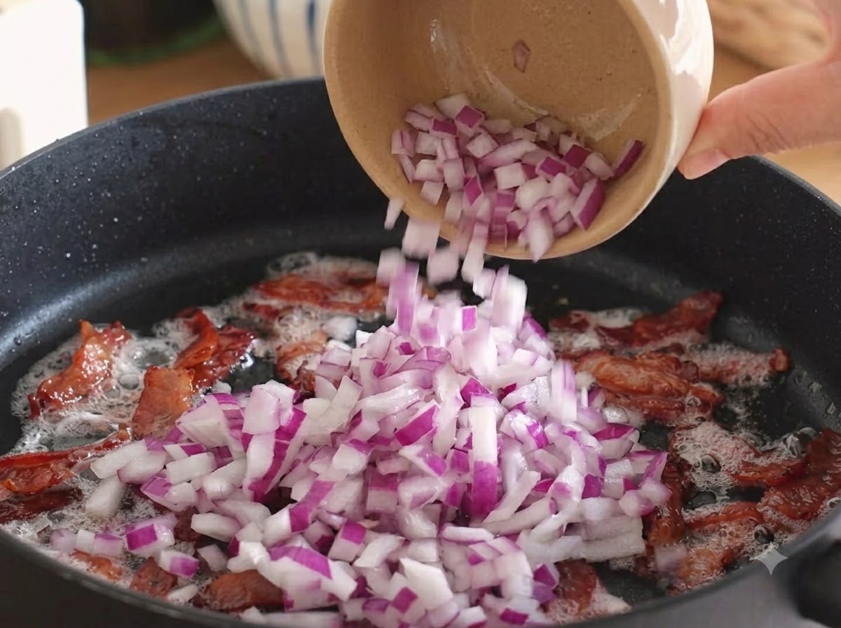 Cipolle rosse tagliate a cubetti versate nella padella sopra la pancetta cotta.