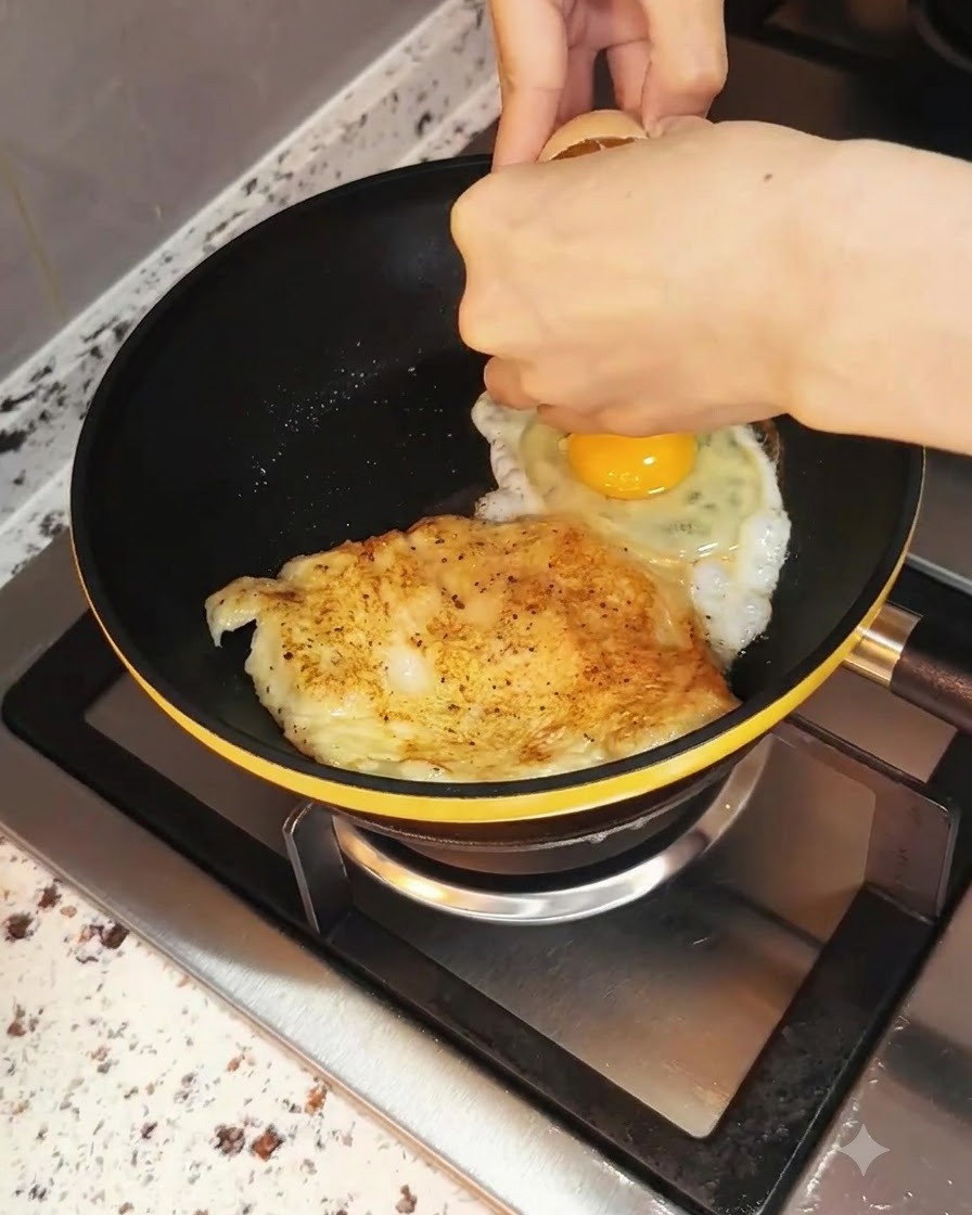 Un uovo rotto allinterno della padella accanto al pollo in cottura.
