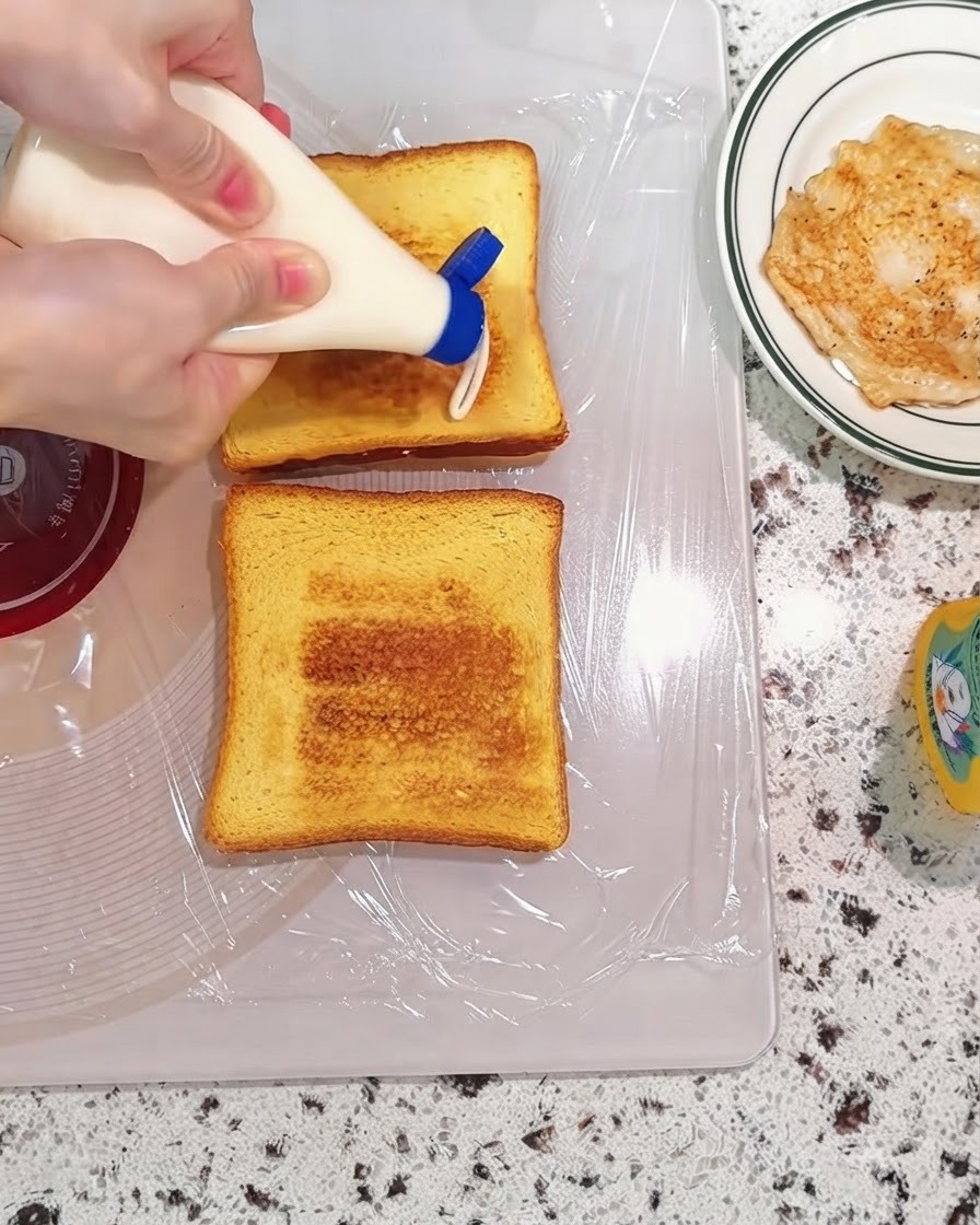 Maionese spremuta da un flacone su fette di pane tostate su un tagliere.