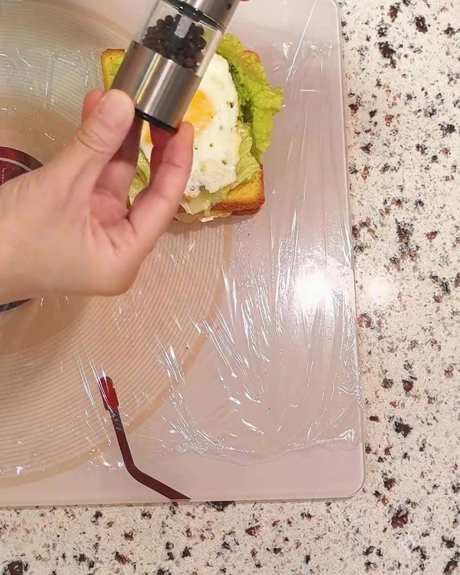 Una mano che tiene un macinapepe e sparge pepe nero sopra luovo fritto.