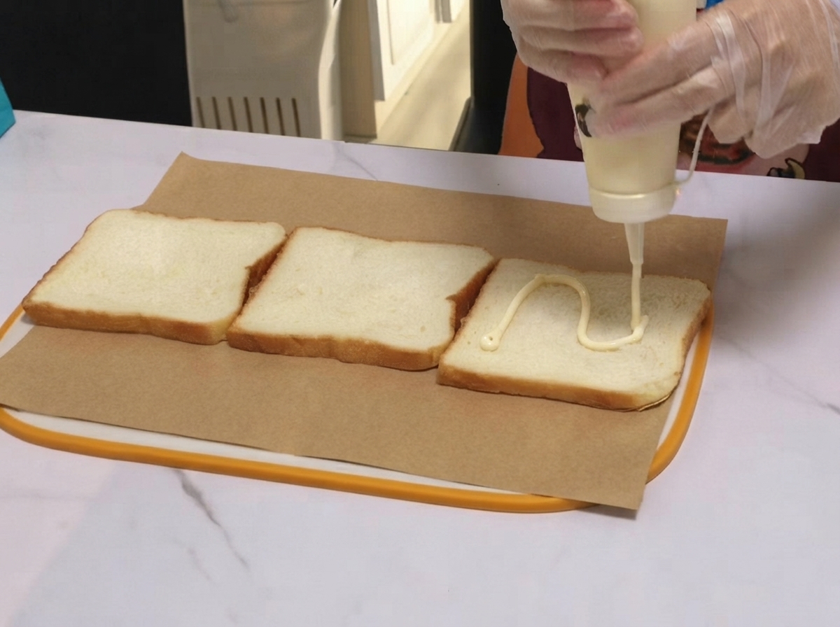 Condimento bianco erogato a linee ondulate su una fetta di pane da toast adagiata sulla carta da forno.