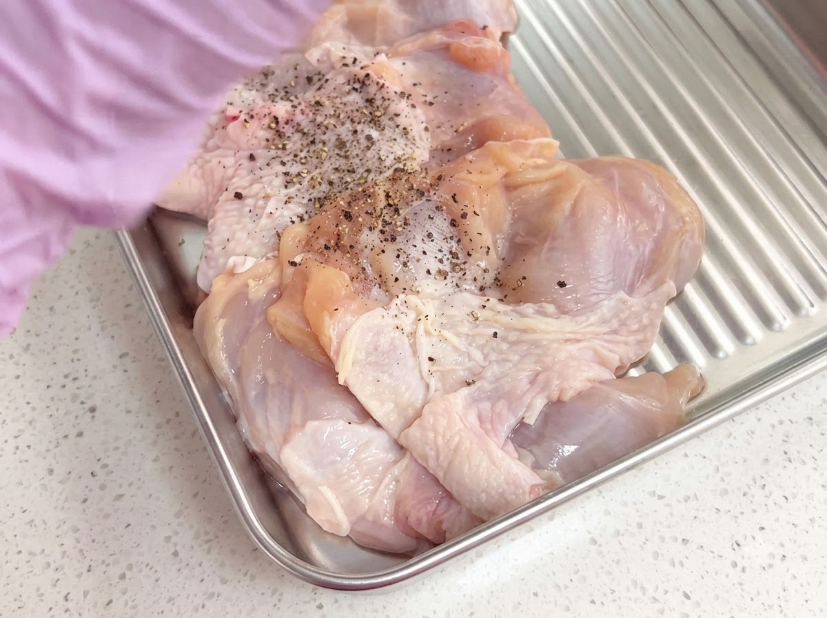 Cosce di pollo disossate condite con pepe nero macinato fresco allinterno di un vassoio di metallo.