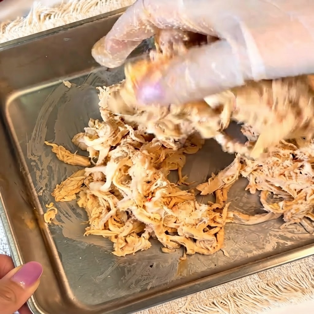 Mani con guanti che mescolano il pollo sfilacciato condito dentro un contenitore di metallo.