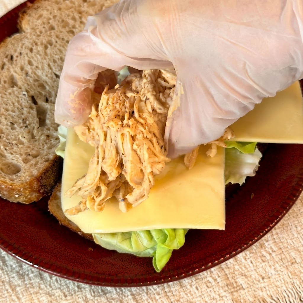 Guanti che dispongono una porzione di pollo sfilacciato condito sopra lo strato di formaggio.