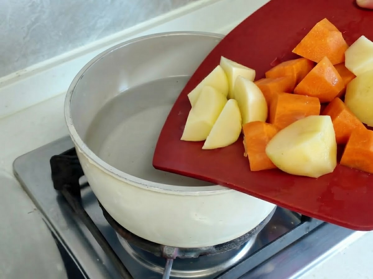Pezzi di patate e carote che bollono allinterno di una pentola su un fuoco caldo.