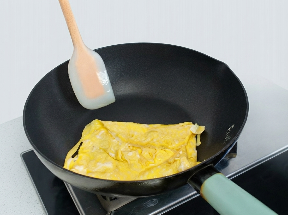 Frittata di uova parzialmente piegata in una padella modellata con una spatola in silicone.