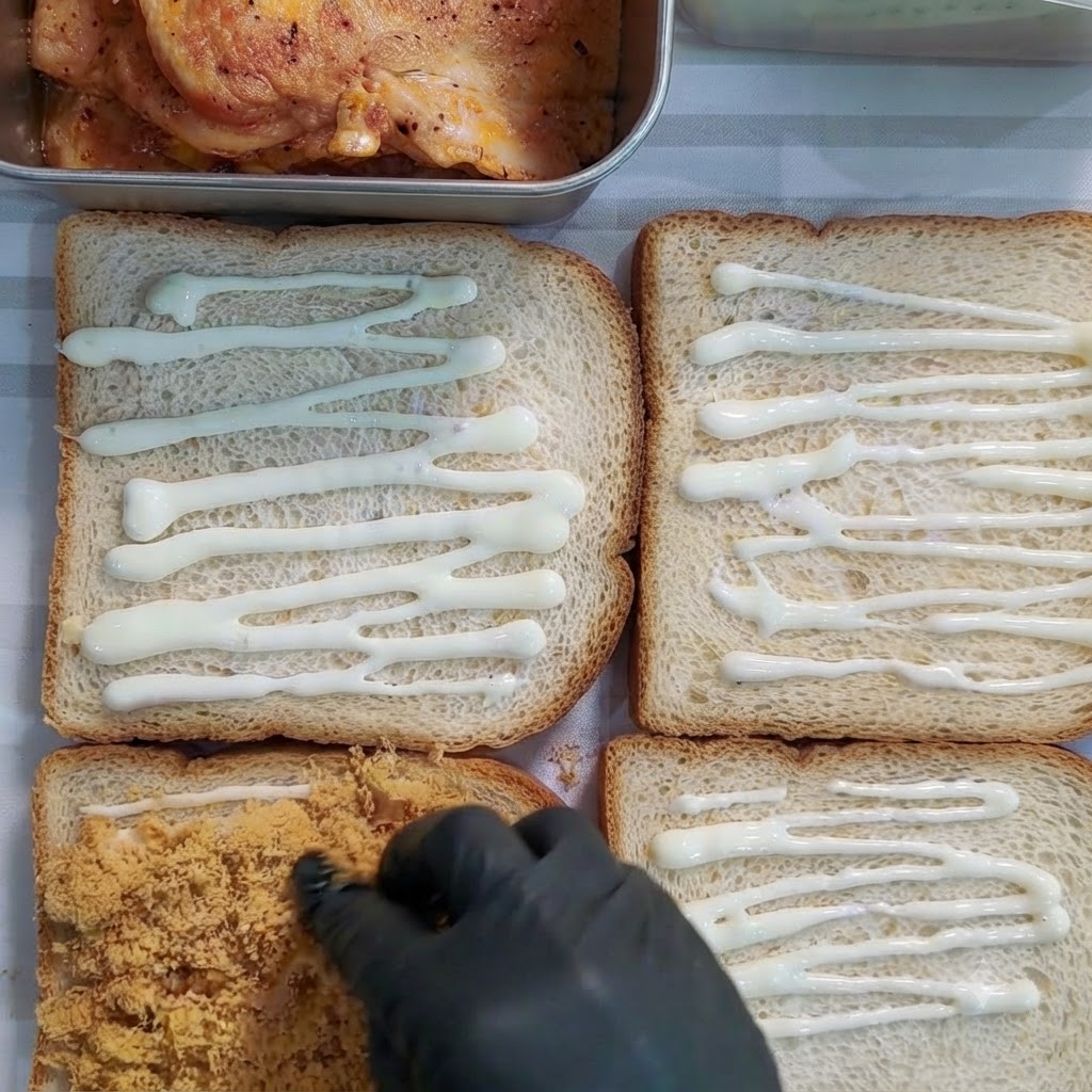 Mano guantata che distribuisce floss di maiale dorato su una fetta di pane coperta di salsa.