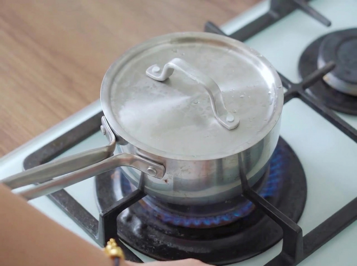 Una pentola coperta su un piano cottura acceso con vapore che fuoriesce, mentre cuoce il petto di pollo.