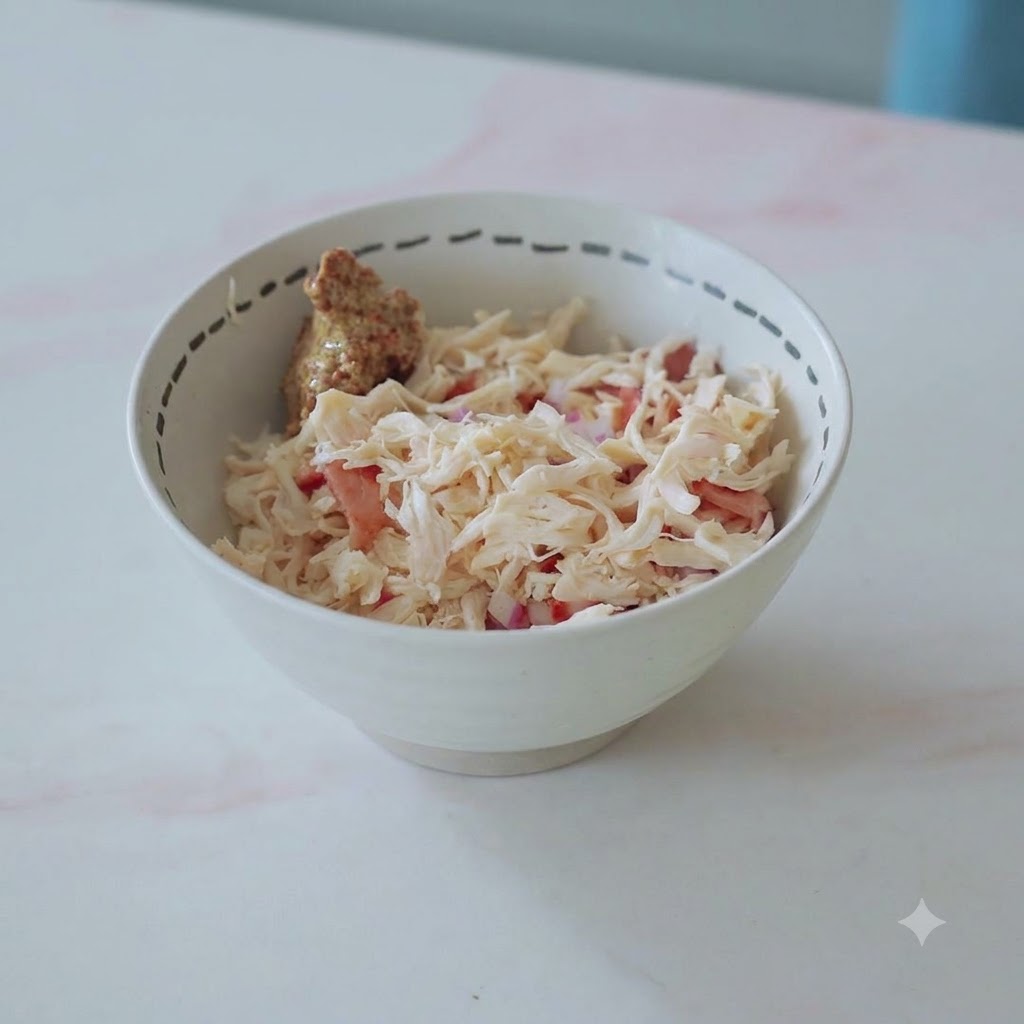 Una ciotola riempita con pollo sfilacciato, pancetta, cipolle e un cucchiaio di senape pronti per essere mescolati.