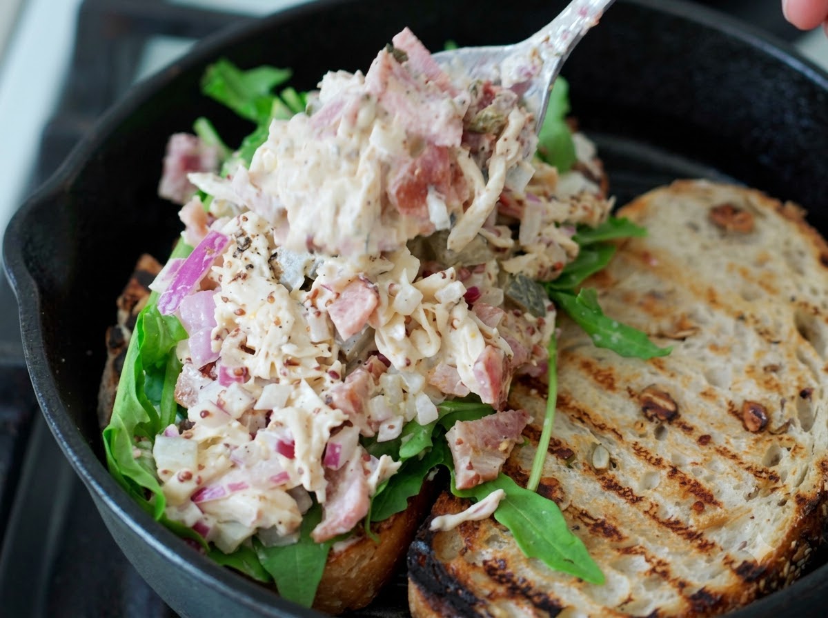 Un cucchiaio di insalata di pollo sfilacciato posto sopra la rucola fresca verde su una fette di panino.