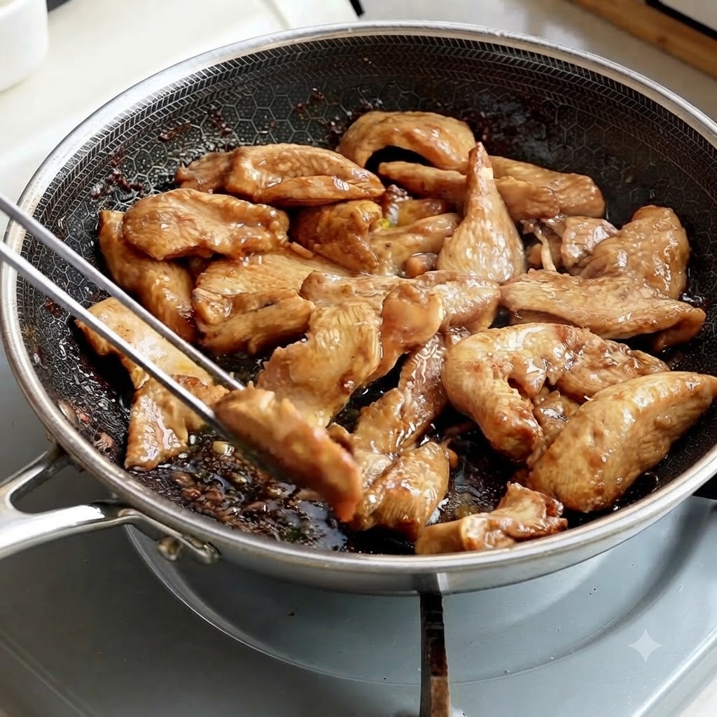 Pinze di metallo che raccolgono strisce di pollo cotto da una padella.