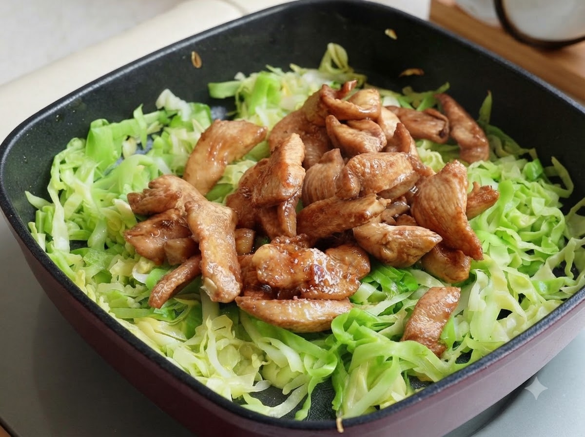 Strisce di petto di pollo cotte poste sopra il cavolo sminuzzato nella padella, divise in due sezioni.