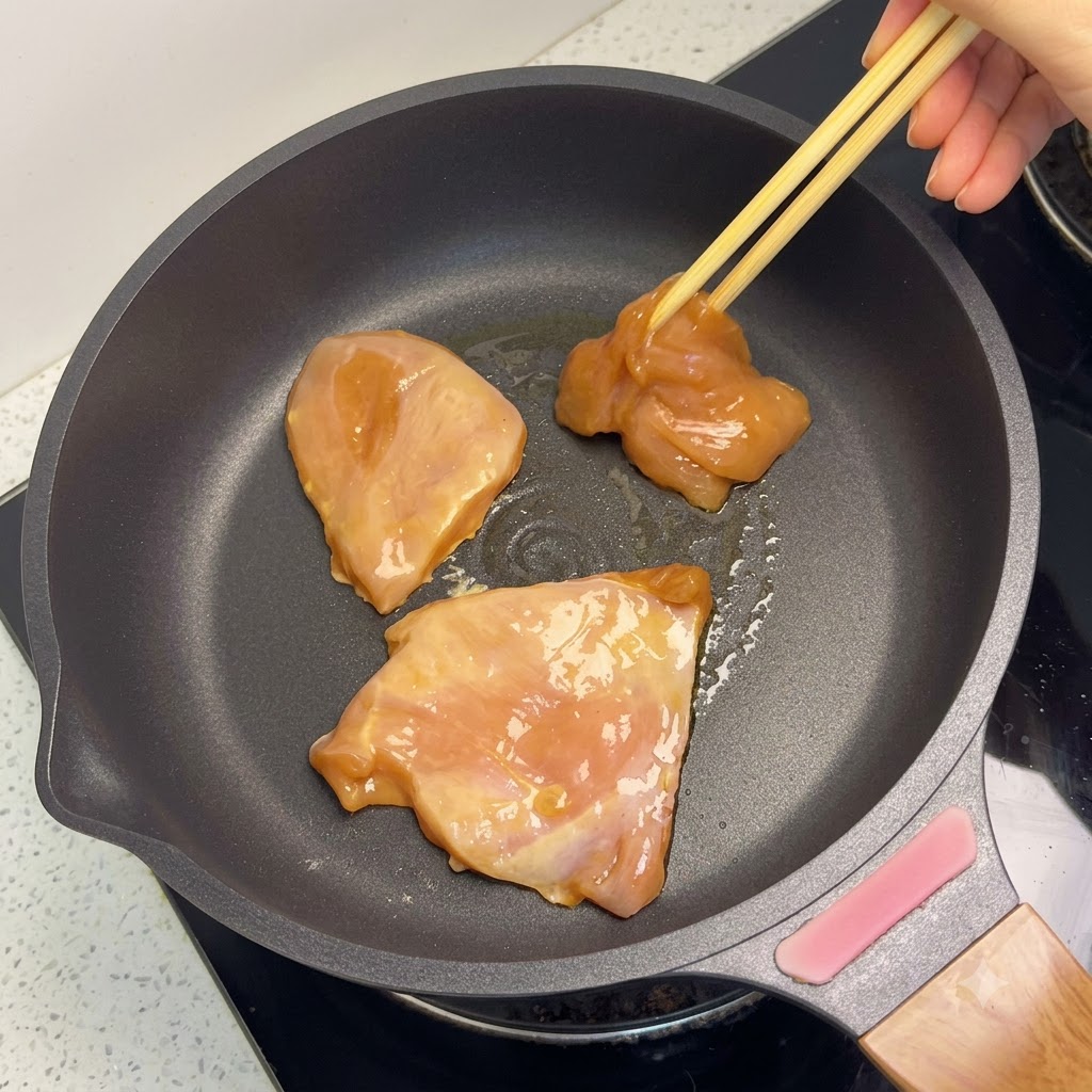 Pezzi di petto di pollo dorati che cuociono in una padella.