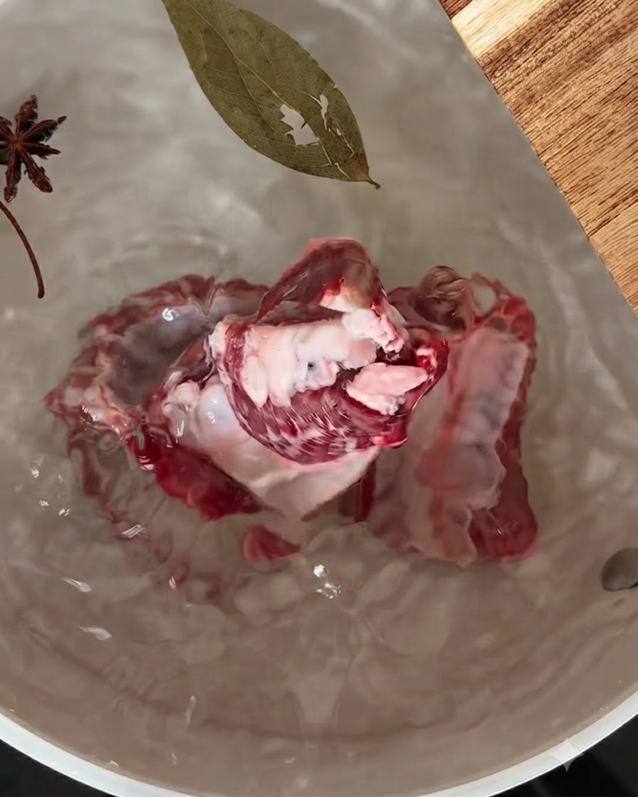 Costine di maiale che sobbollono in una pentola dacqua con anice stellato e una foglia di alloro che galleggia sopra.