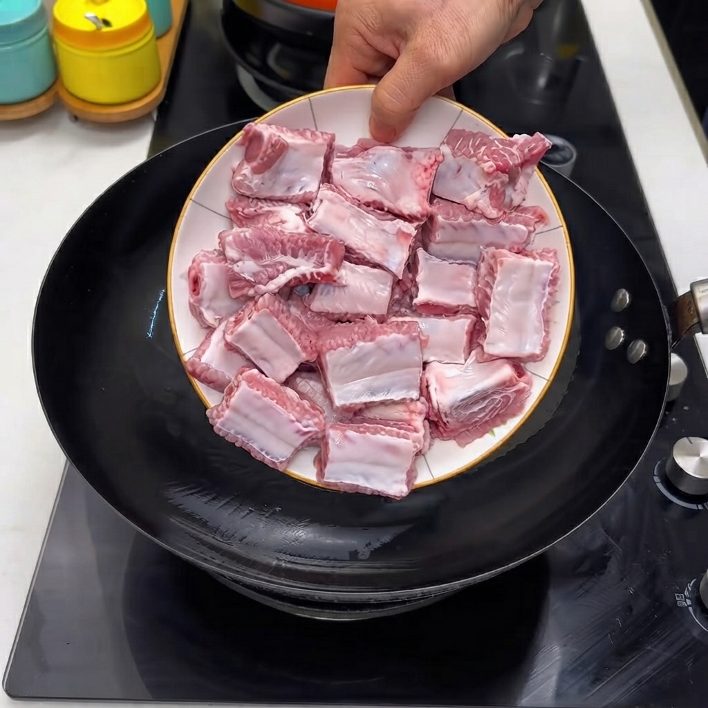Costine di maiale crudo versate da un piatto bianco in un wok nero caldo.