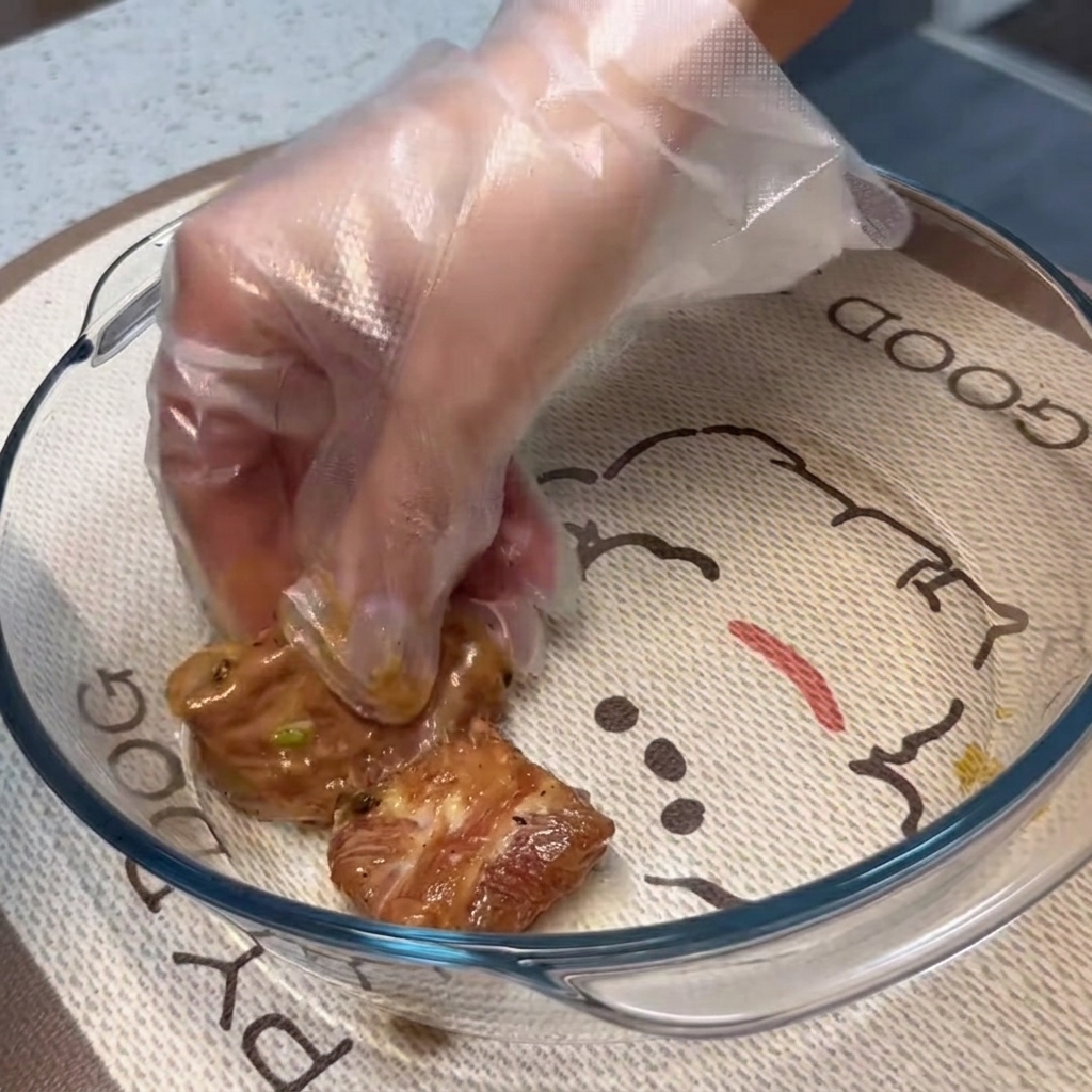 Costine di maiale marinate disposte in uno strato piatto e singolo allinterno di una teglia di vetro trasparente.