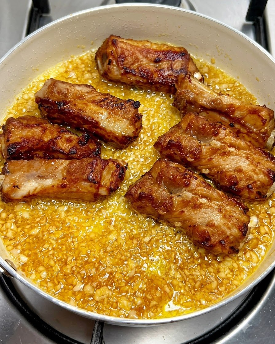 Costine di maiale fritte e dorate disposte ordinatamente allinterno di una padella piena di salsa al burro e aglio frizzante.