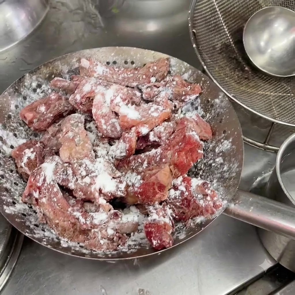Costine di maiale marinate adagiate allinterno di un colino metallico con un visibile strato bianco di amido.
