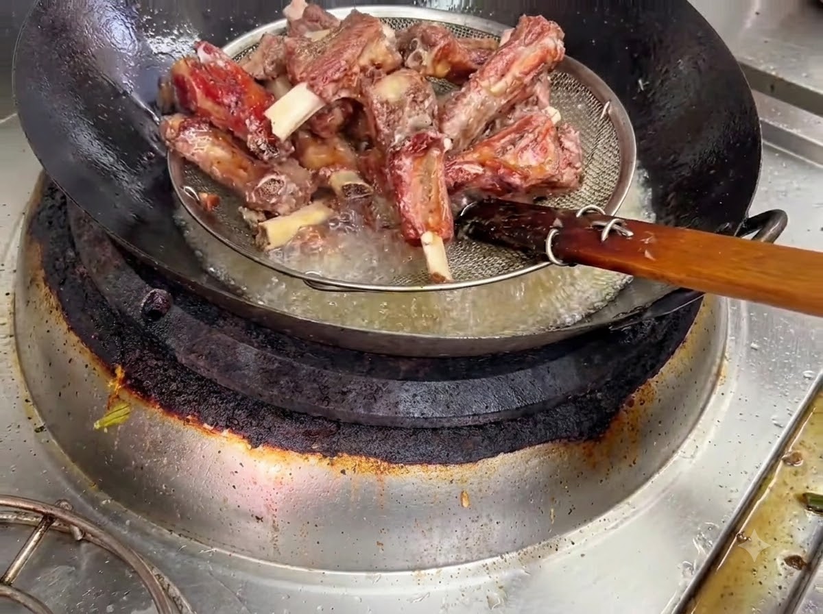 Costine di maiale fritte sollevate dallolio bollente tramite un cestino scolapasta in filo metallico.
