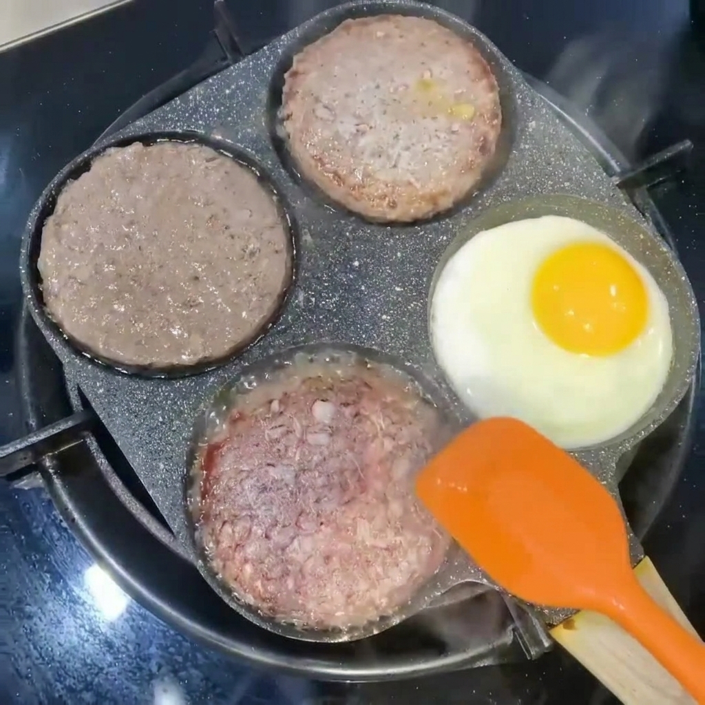 Hamburger girati con una spatola arancione accanto a un uovo in cottura in una sezione della padella.