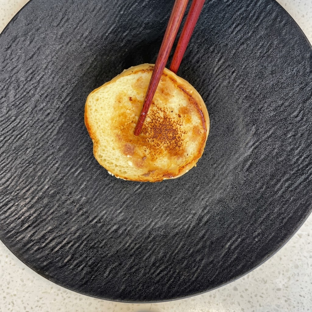 Una metà di panino da burger tostato poggiata su un piatto nero strutturato con delle bacchette.