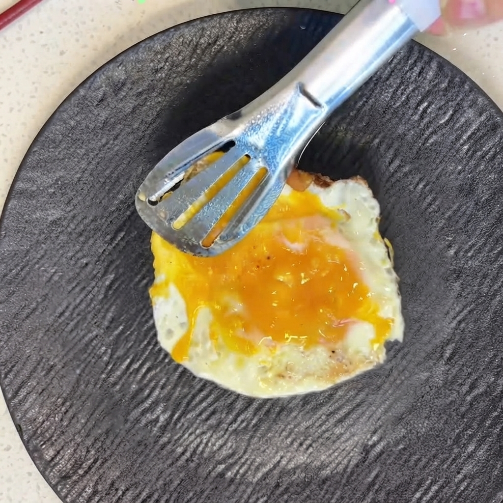 Un uovo fritto di fresco posizionato con cura sopra i pomodori affettati usando delle pinze di metallo.