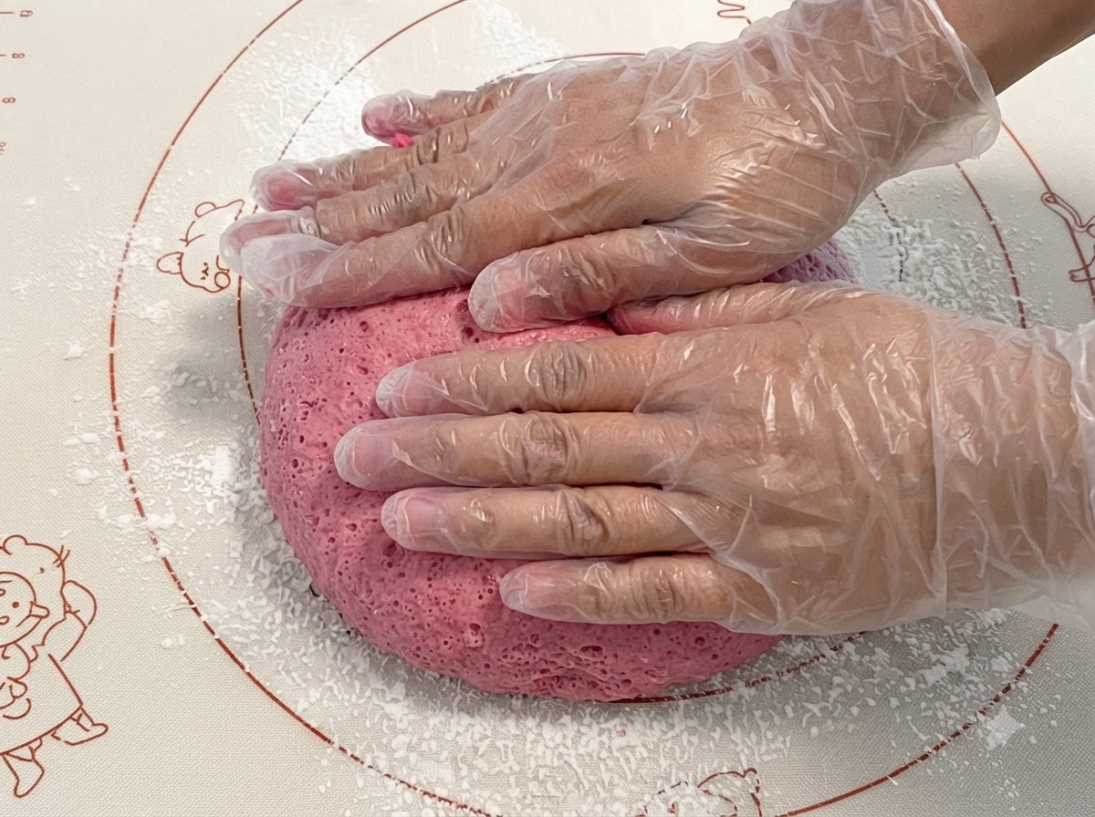 Impasto rosa fermentato premuto e impastato su un tappetino in silicone.