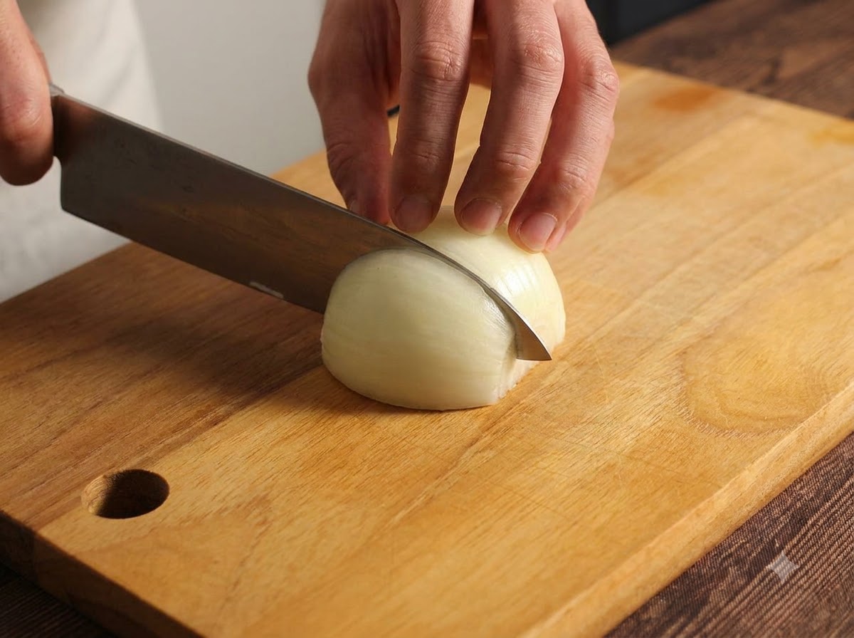 Una cipolla tagliata e tritata con cura su un tagliere di legno usando un coltello da cucina.