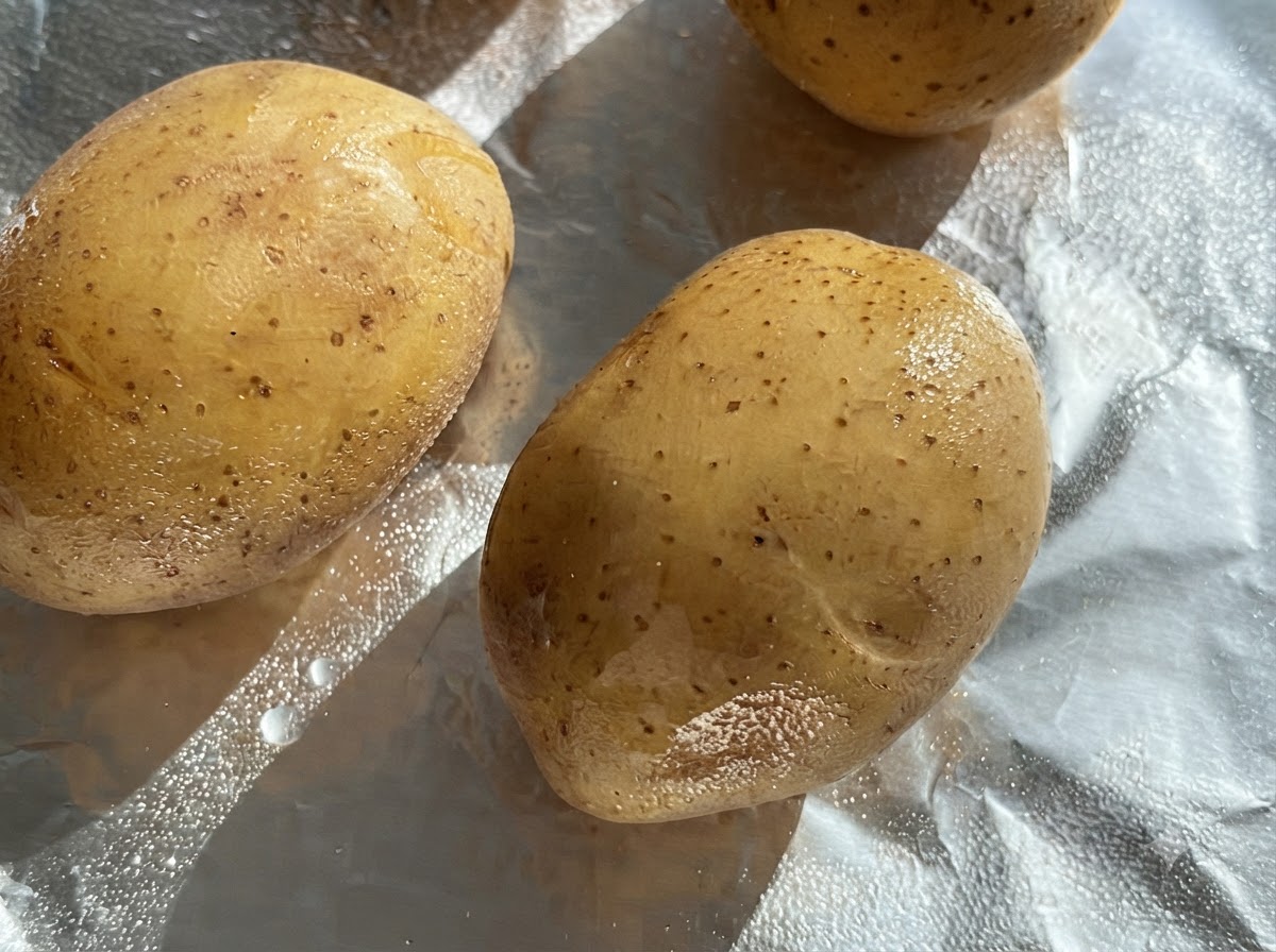 Patate intere crude spennellate dolio su un foglio di carta stagnola.