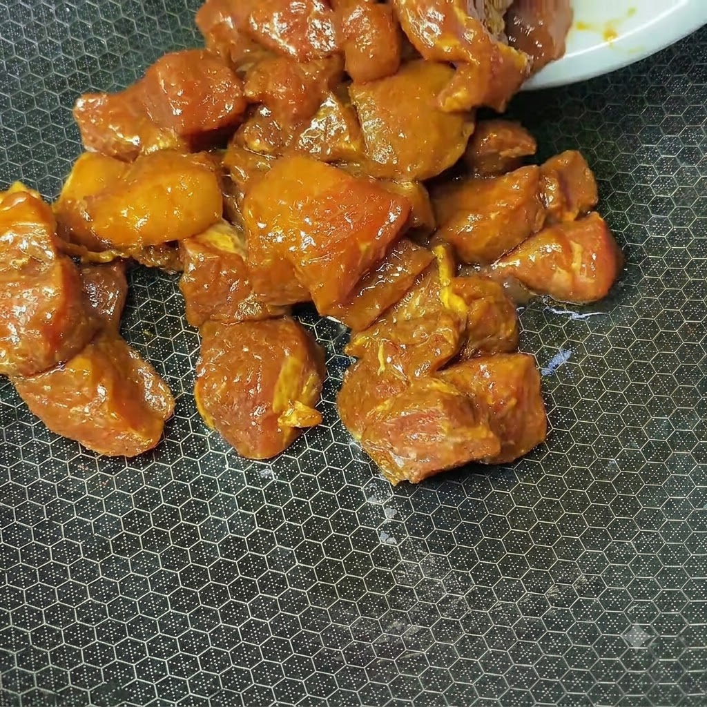 Cubetti di maiale marinati marrone rossastro in cottura allinterno di un wok caldo e strutturato.
