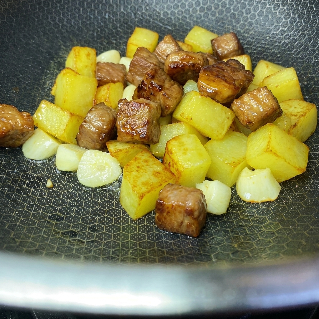 Cubetti di patate croccanti dorate e cubetti di maiale rosolati uniti insieme allinterno di un wok.