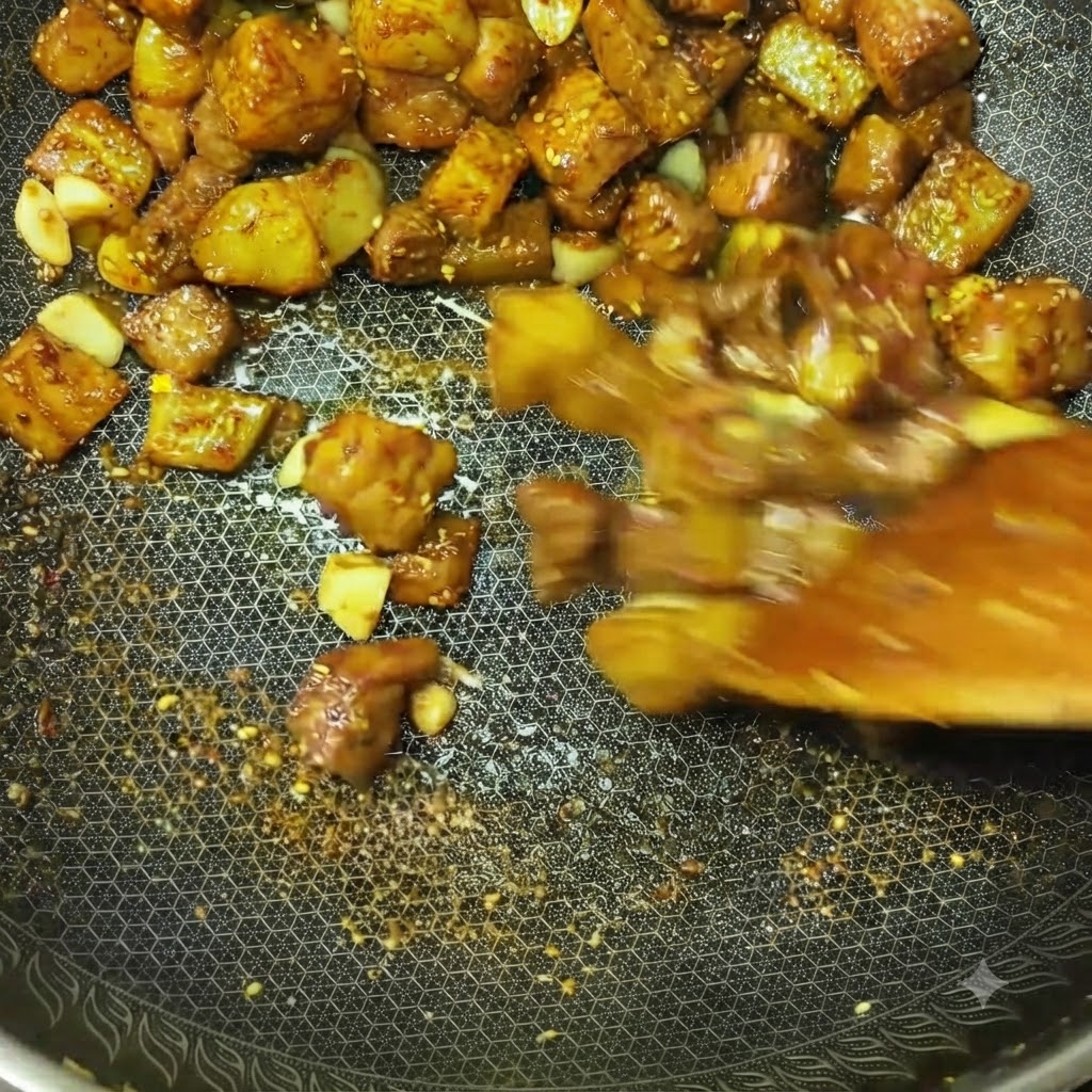 Cubetti di carne e pezzi di patate saltati rapidamente in un wok con spezie e condimenti visibili.