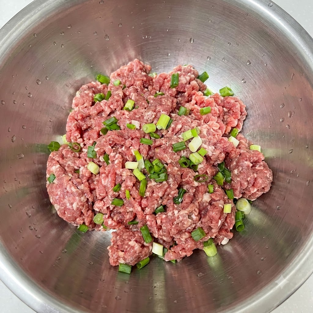 Cipollotti freschi tritati disposti sopra alla carne macinata in una ciotola di acciaio inossidabile.