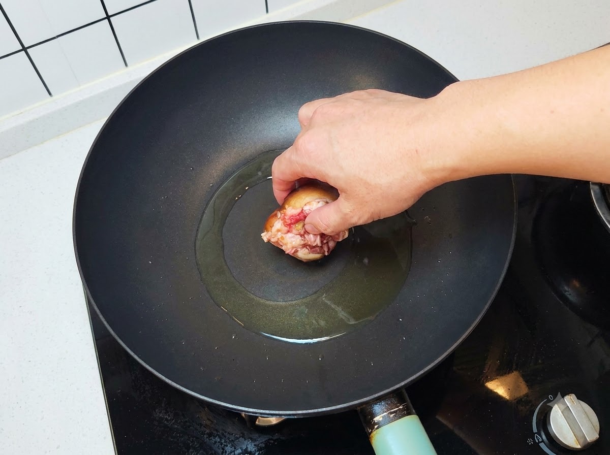 Un fungo ripieno viene posizionato con la carne rivolta verso il basso in un wok caldo e oliato.