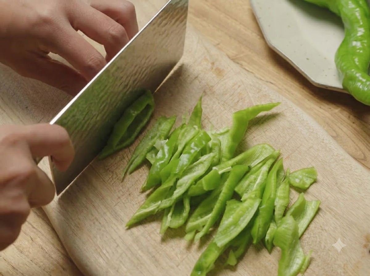 Peperoncini verdi a spirale tagliati a pezzi obliqui su un tagliere di legno con una mannaia.