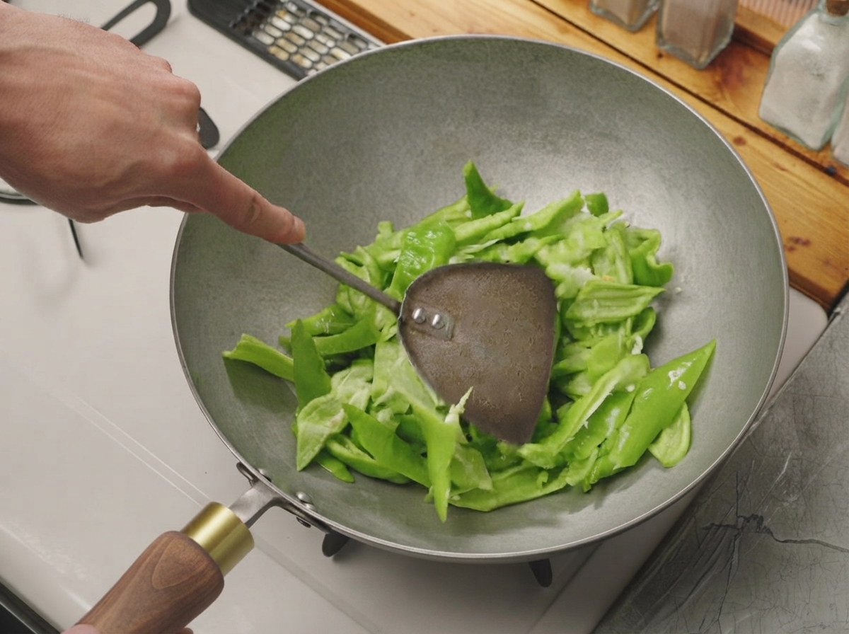 Peperoncini verdi tagliati mescolati con una spatola di metallo in un wok caldo e asciutto.
