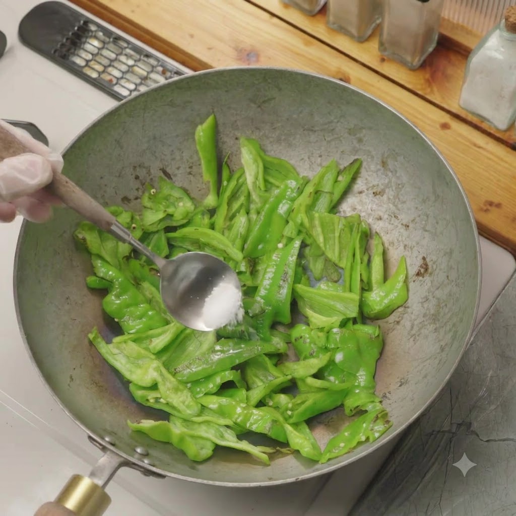 Un cucchiaio di sale aggiunto ai peperoncini verdi tagliati che cuociono a secco in un wok.