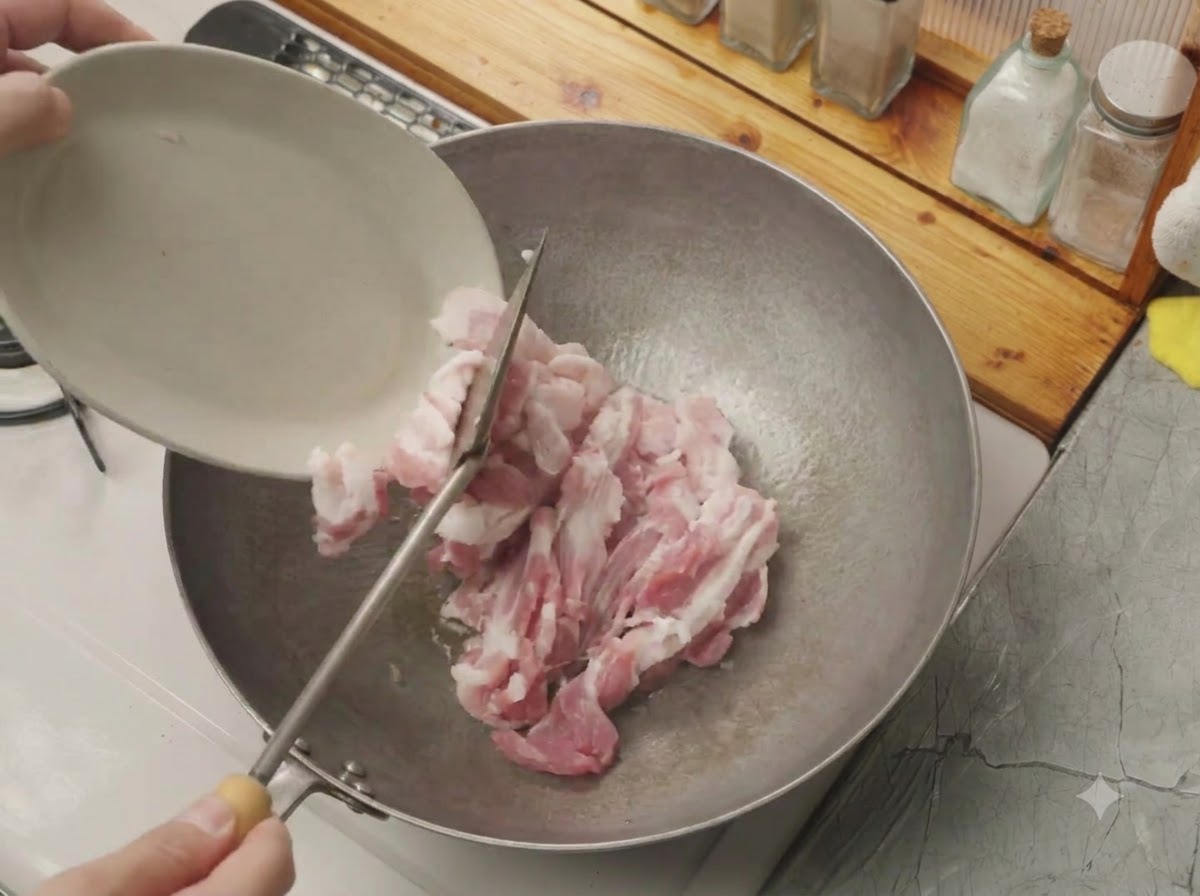 Pancetta di maiale cruda affettata fatta scivolare da un piattino bianco in un wok caldo.