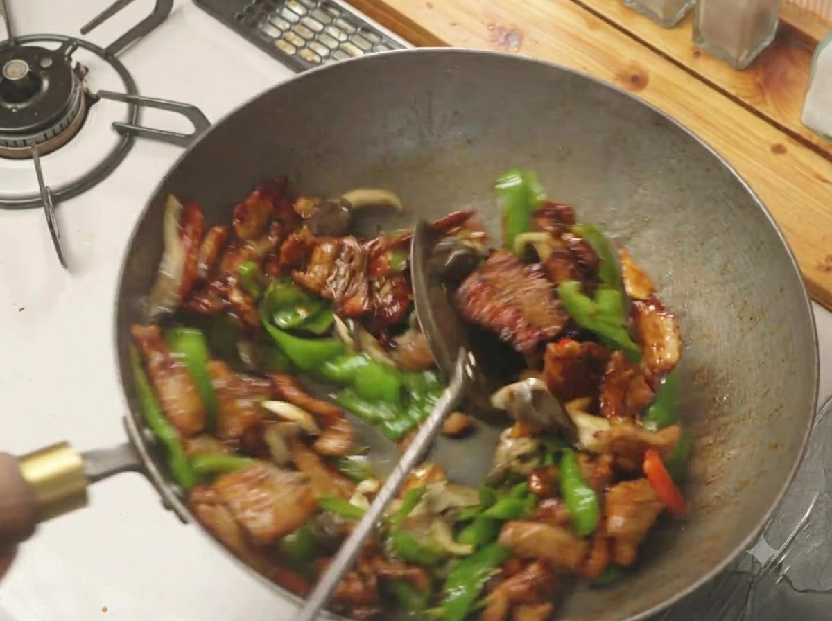 Una spatola che mescola peperoncini verdi, funghi e pancetta di maiale insieme in un wok caldo.